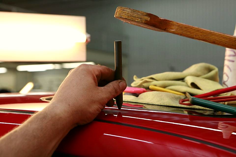 Hand met uitdeukgereedschap op een rode carrosserie